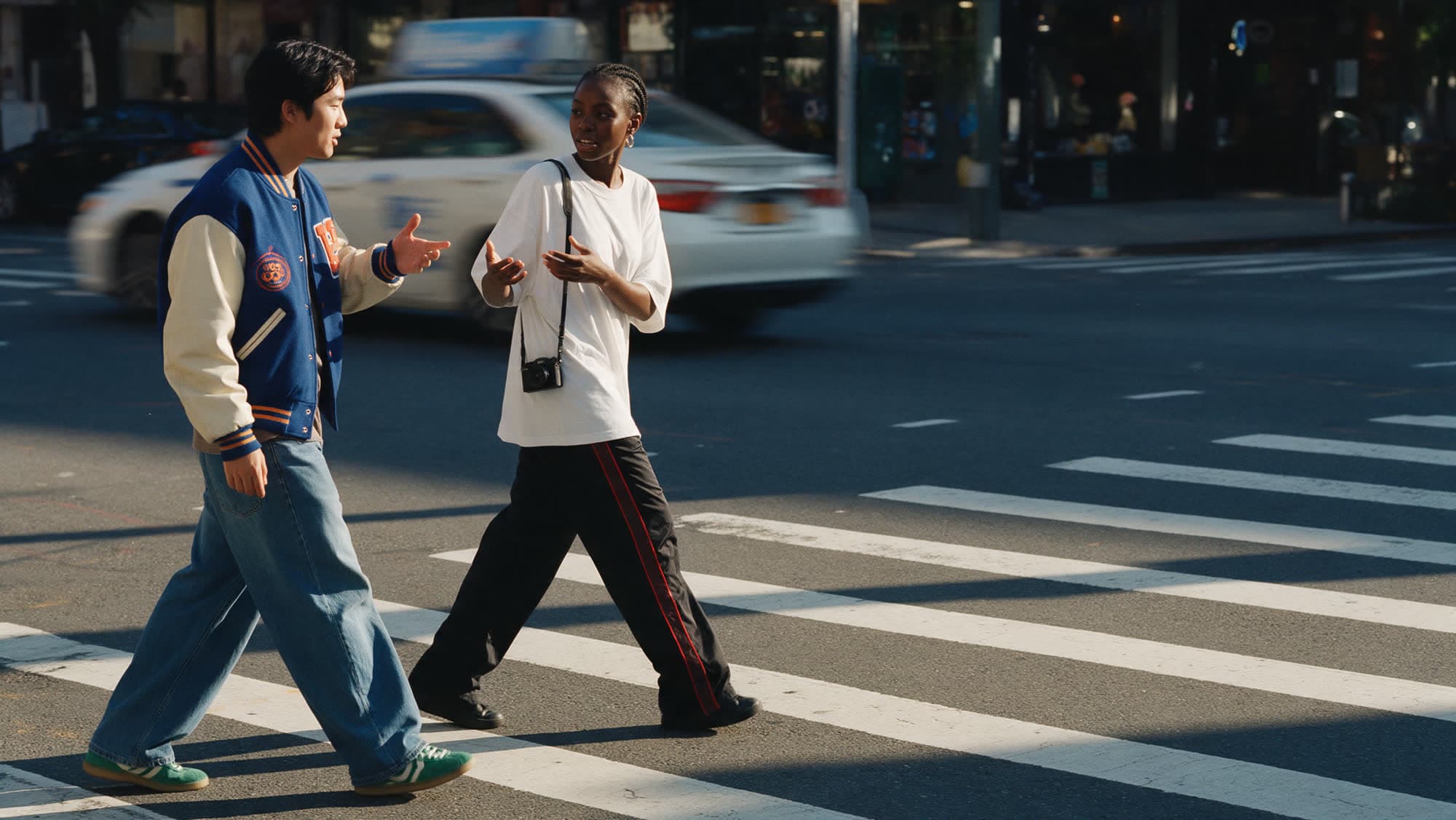 Two friends crossing a city street mid-conversation in late-afternoon light