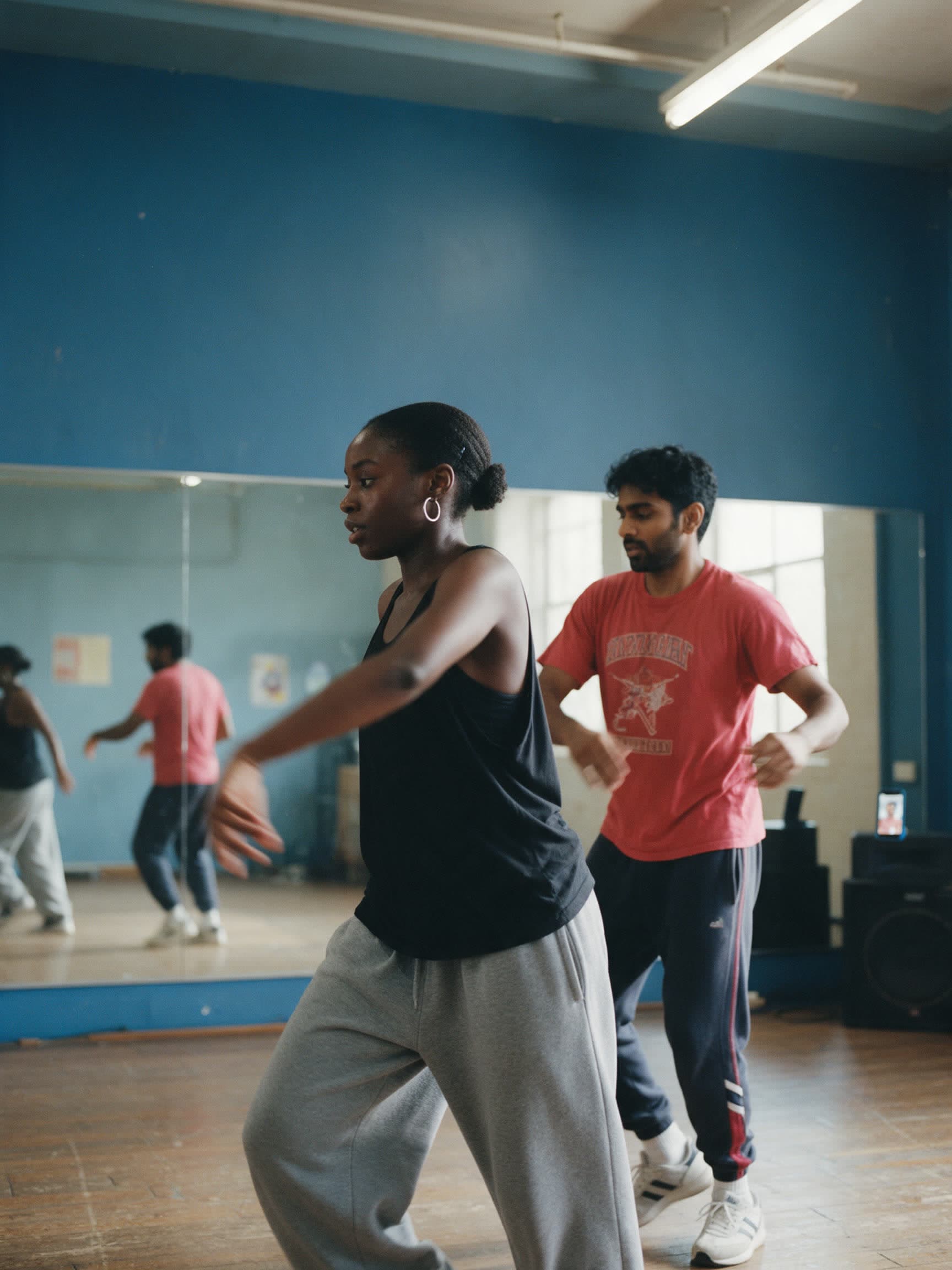 Two friends dancing in a rehearsal studio, caught mid-step