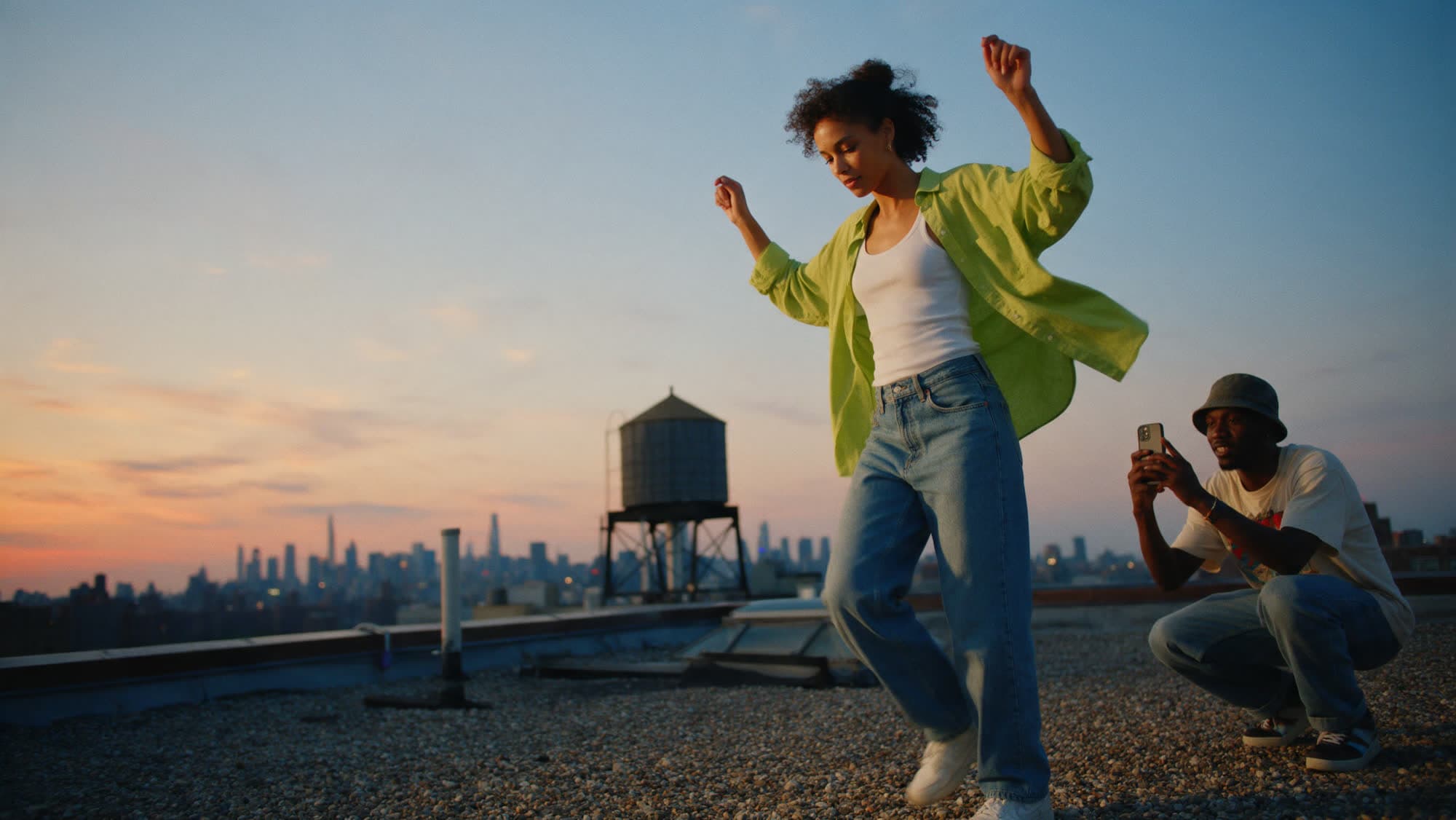 A creator dancing on a city rooftop at sunset while a friend films on a phone